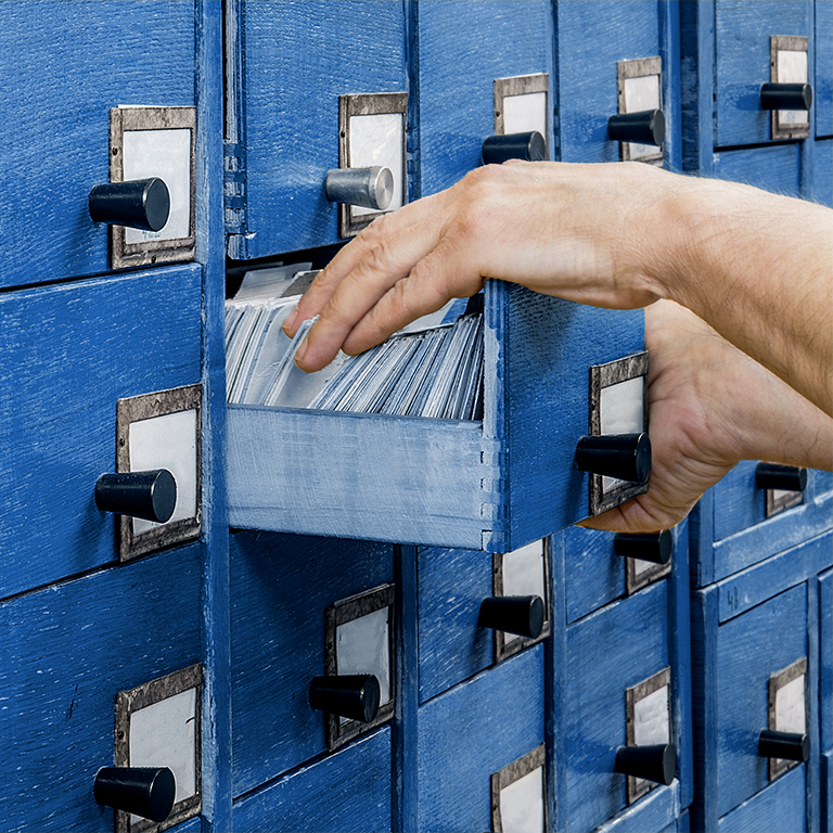 Hands going through cards from an old wooden card catalogue cabinet. Front view. Information archive background concept.